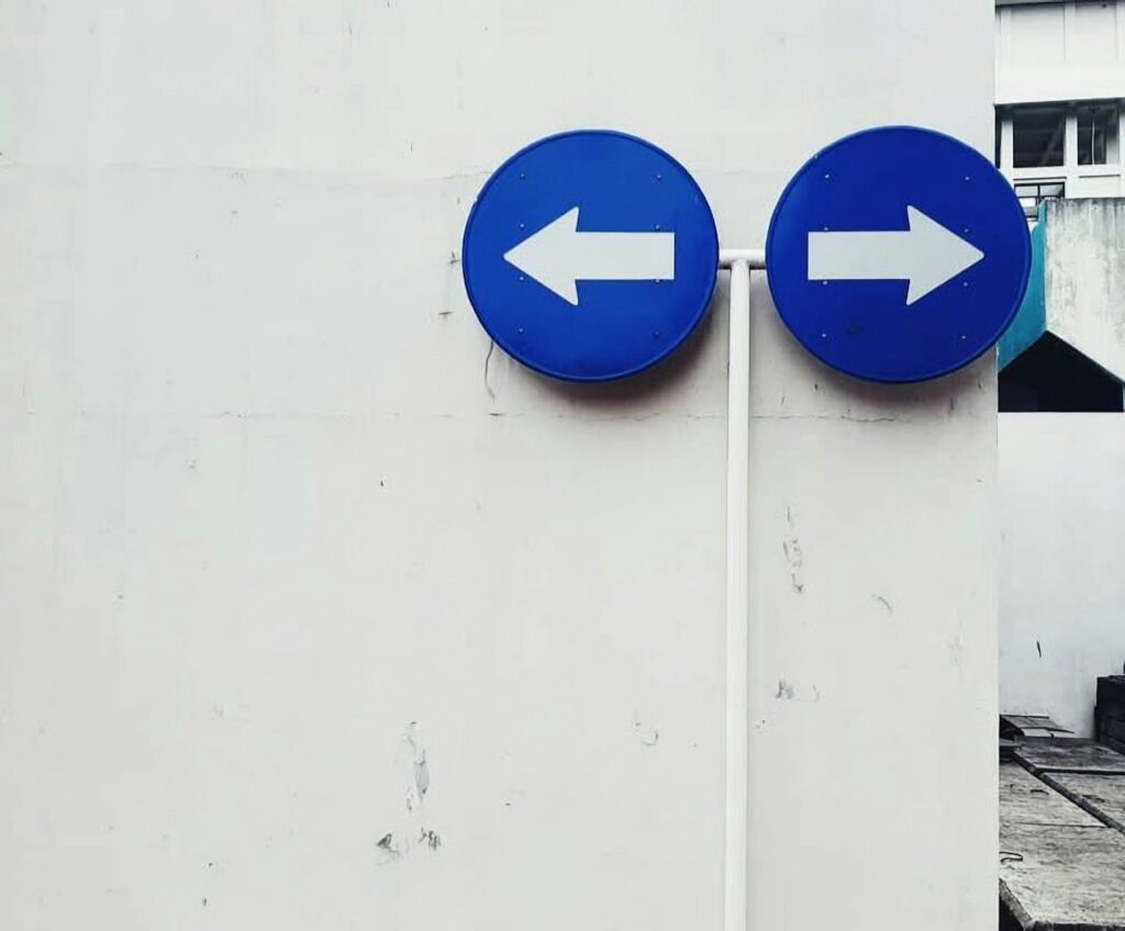Two blue signs pointing in opposite directions on a white wall